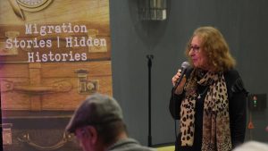 Claudette standing with a microphone with a hidden histories banner behind her